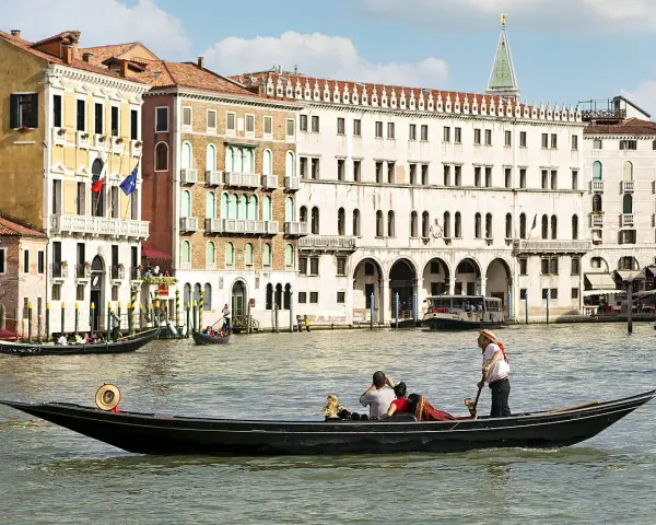 Gondola con turisti e gondoliere, sullo sfondo palazzi storici e altre barche tipiche veneziane.