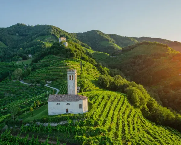 Un borgo con una chiesetta e campanile tra colline vitate, un esempio di cosa vedere nei dintorni di Treviso per un paesaggio incantevole.