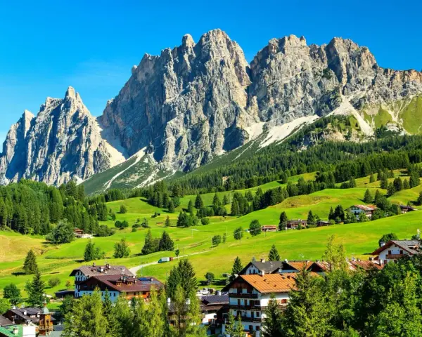 Un viaggio da Venezia a Cortina: verdi pascoli, boschi rigogliosi e imponenti vette dolomitiche incorniciano un villaggio alpino.