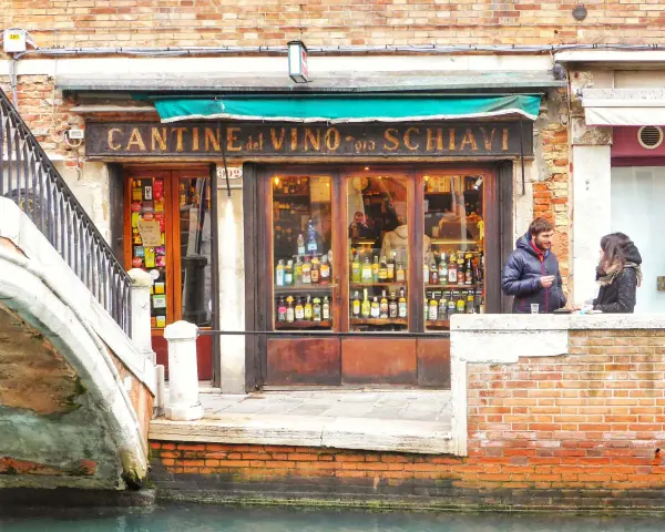 Coppia davanti a una delle tipiche osterie a Venezia, con bottiglie di vino in esposizione.