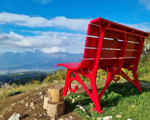 La panchina gigante sul Nevegal, rossa e imponente, domina un panorama mozzafiato di montagne e vallate sotto un cielo azzurro.