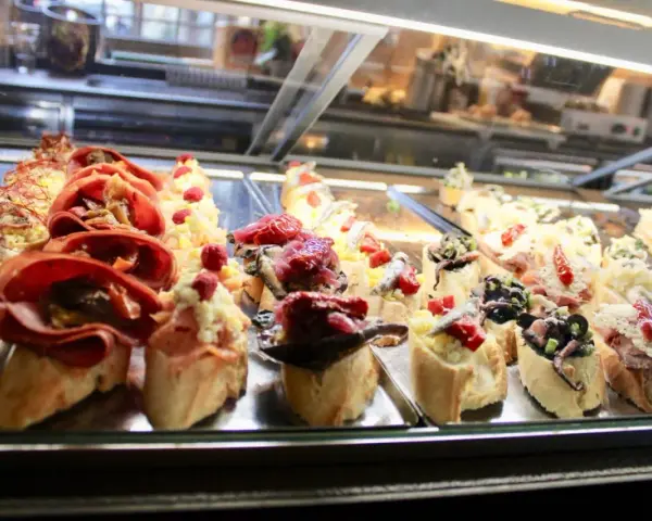 Assortimento di cicchetti in una vetrina di un'osteria veneziana: crostini con salumi, pesce e verdure.