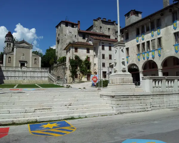Piazza con scalinata, chiesa e castello: ecco cosa vedere a Feltre. Stendardi gialli decorano gli edifici storici.