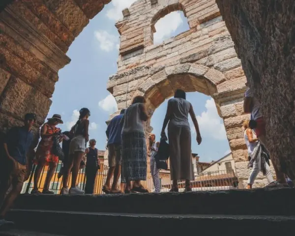 Turisti esplorano l'Arena di Verona, un'antica struttura che ricorda il Colosseo, sotto un cielo azzurro.