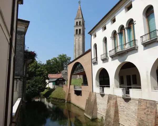 Canale e campanile a Oderzo, cosa vedere: un'elegante facciata bianca con portici e balconi si affaccia sull'acqua, con un ponte ad arco in mattoni.