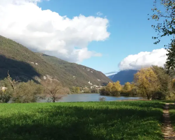 Sentiero per passeggiate in montagna Veneto, con lago, colline verdi e cielo azzurro con nuvole bianche.