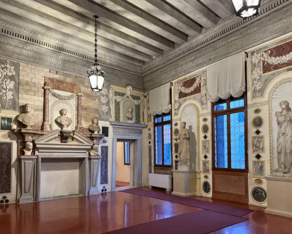 Interni del Palazzo Grimani: busti, statue, camino e finestre decorate in un salone sontuoso.