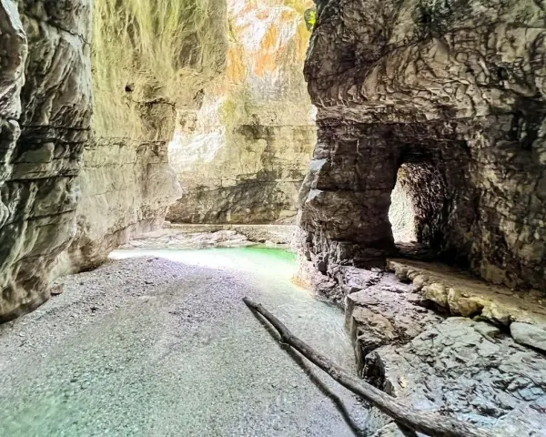 Gola rocciosa con acqua cristallina che ricorda il lago del Mis. Un sentiero scavato nella roccia conduce verso un'apertura luminosa.