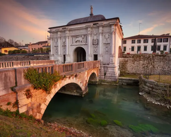 Porta San Tomaso a Treviso, un'idea per cosa fare a Treviso nel weekend. Un ponte in mattoni attraversa un canale con acqua verde.