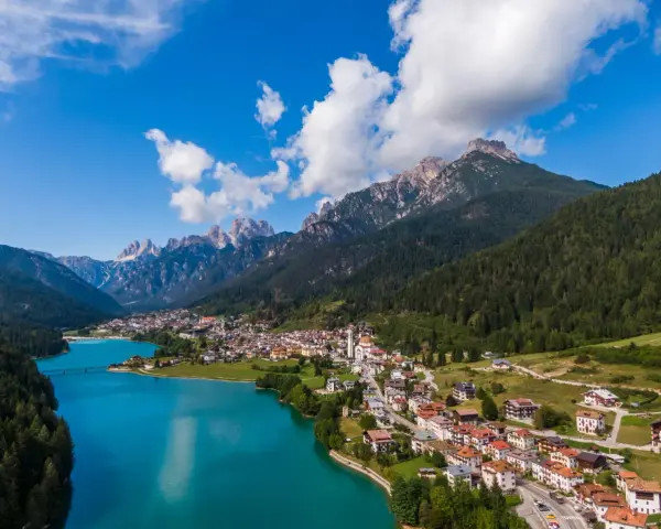 Vista aerea del **lago Auronzo di Cadore** con le montagne sullo sfondo e il paese che si affaccia sull'acqua turchese.