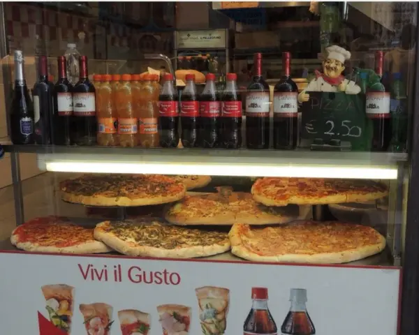 Vetrine con pizze, bottiglie di vino e bibite, un cartello "PIZZA DA € 2.50" e un cuoco decorativo. Sembra un ottimo posto per trovare le migliori pizzerie a Venezia.
