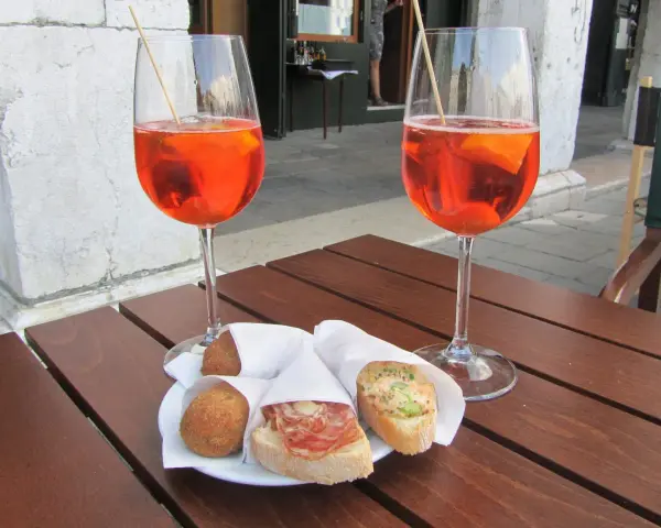 Due calici di Spritz e cicchetti, un classico per gli aperitivi a Venezia, su un tavolino di legno.