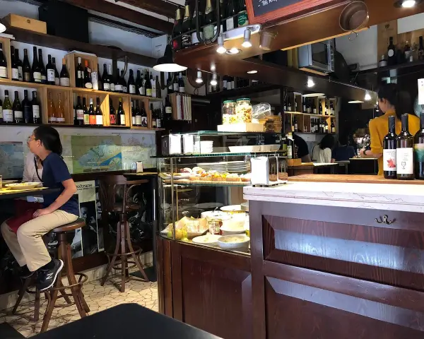 Interno di un'osteria al cicheto a Venezia, con bottiglie di vino, cibi in vetrina e persone sedute al bancone.