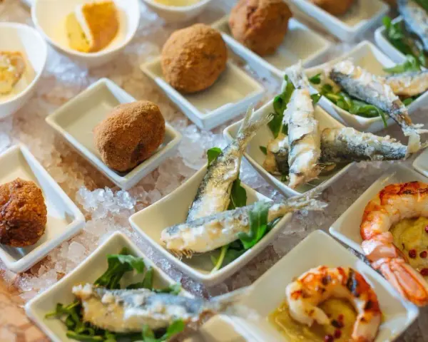 Assaggio di prodotti tipici veneziani: crocchette dorate, sarde fritte e gamberi grigliati, presentati su un letto di ghiaccio.