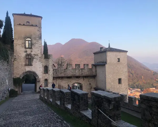 Antico borgo di Cison di Valmarino con torri e mura di pietra, sullo sfondo colline autunnali.