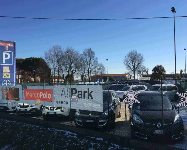 Parcheggio Marco Polo, con bus navetta gratuito per l'aeroporto. Auto parcheggiate dietro una recinzione con decorazioni a fiocco di neve.