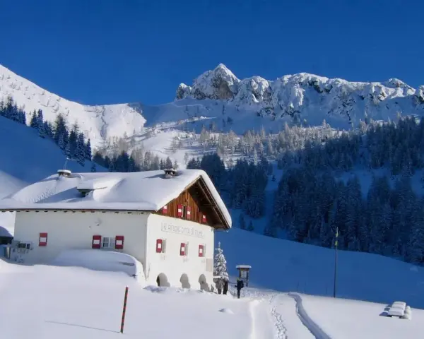 Rifugio innevato nelle Dolomiti, ideale per ciaspolate invernali. Montagne maestose e boschi coperti di neve.