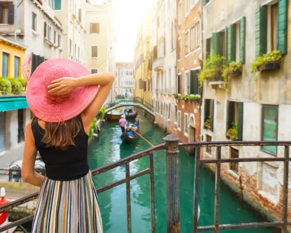 Donna con cappello rosa ammira un canale a Venezia, con gondole e palazzi storici. Un'esperienza da vivere a piedi, tra Santa Lucia e Piazza San Marco.