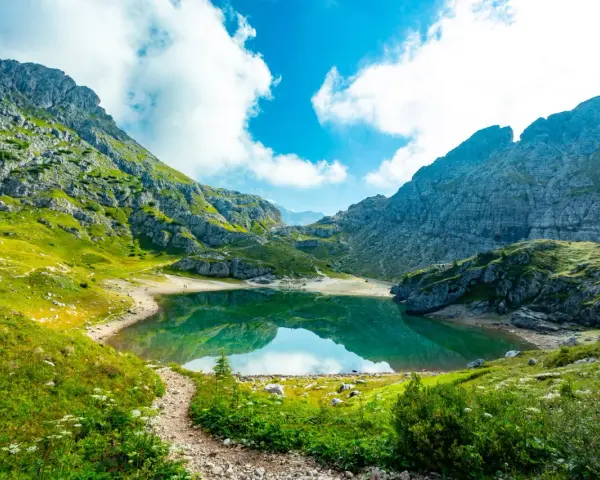 Sentiero panoramico verso un lago alpino turchese, incorniciato da montagne maestose. Un vero gioiello dell'alta via Dolomiti più bella.