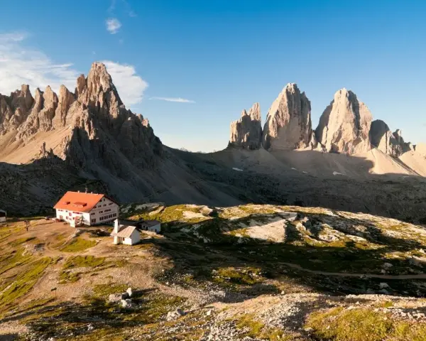Rifugio con tetto rosso e montagne imponenti, un'oasi di pace tra i rifugi Dolomiti Bellunesi facili, ideale per un'escursione panoramica.