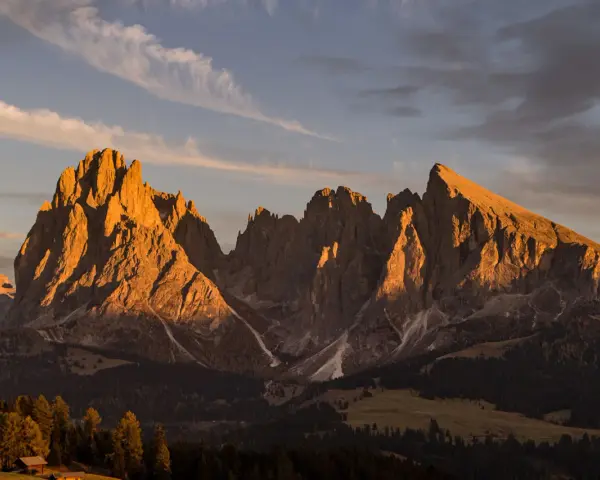 Le maestose **Dolomiti Rosse** illuminate dal sole al tramonto, con cime aguzze e pendii boscosi.