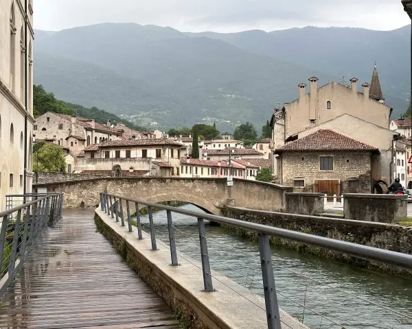 Passeggiata lungo il canale, tra antichi palazzi e ponti in pietra. Ecco cosa vedere a Vittorio Veneto, con le montagne sullo sfondo.