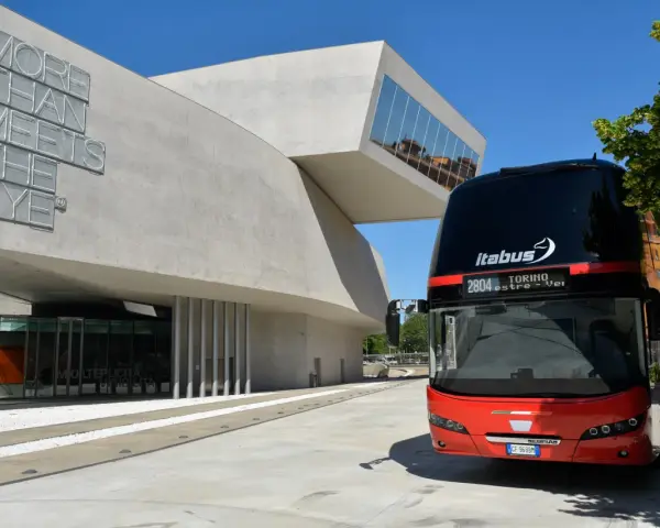 Autobus Itabus rosso e nero davanti a un edificio moderno con la scritta "More Than Meets The Eye". Un viaggio da Verona a Jesolo?