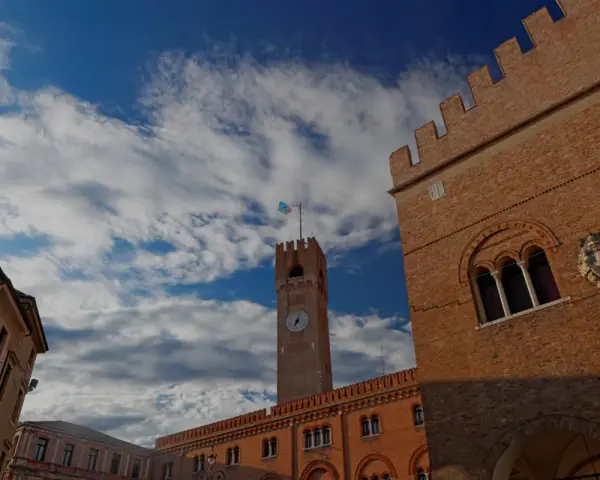 Torre dell'Orologio e palazzi storici a Treviso, un viaggio da Padova a Treviso sotto un cielo azzurro e nuvoloso.