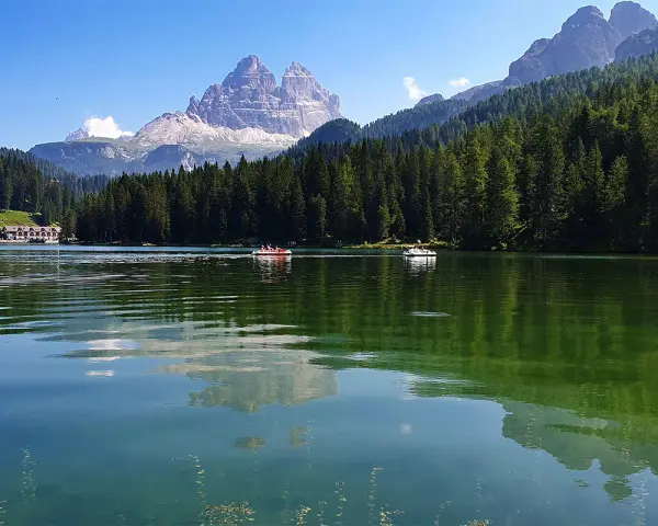 Il **lago di Misurina** incanta con le sue acque verdi e le montagne maestose. Barchette a remi solcano la superficie, riflettendo il cielo azzurro e la foresta di abeti.