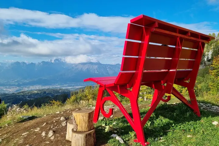 La panchina gigante sul Nevegal, rossa e imponente, domina un panorama mozzafiato di montagne e vallate sotto un cielo azzurro.