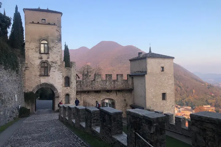 Antico borgo di Cison di Valmarino con torri e mura di pietra, sullo sfondo colline autunnali.