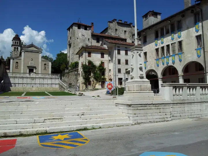 Piazza con scalinata, chiesa e castello: ecco cosa vedere a Feltre. Stendardi gialli decorano gli edifici storici.