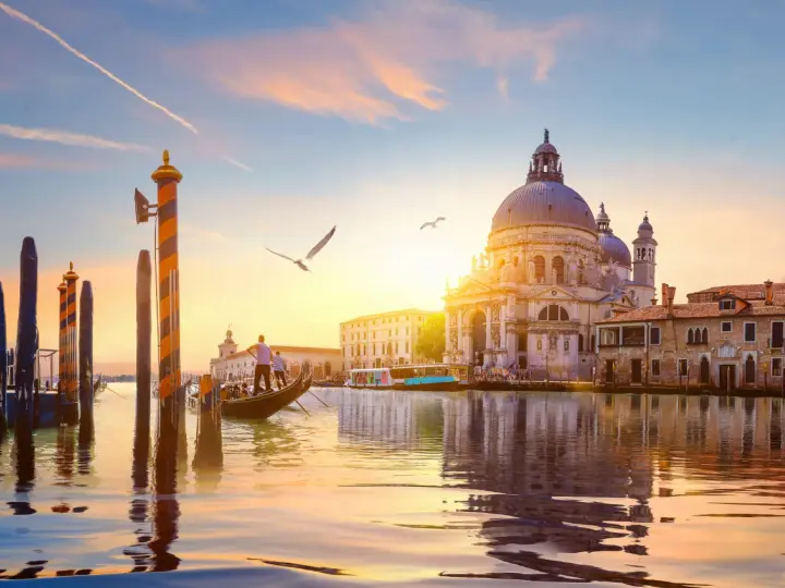 Gondola che scivola sull'acqua al tramonto, con la Basilica di Santa Maria della Salute sullo sfondo. Un'indimenticabile attività a Venezia.