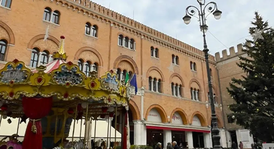 Carosello colorato e albero di Natale in piazza, scorci di cosa vedere a Treviso con palazzi storici e gente che passeggia.