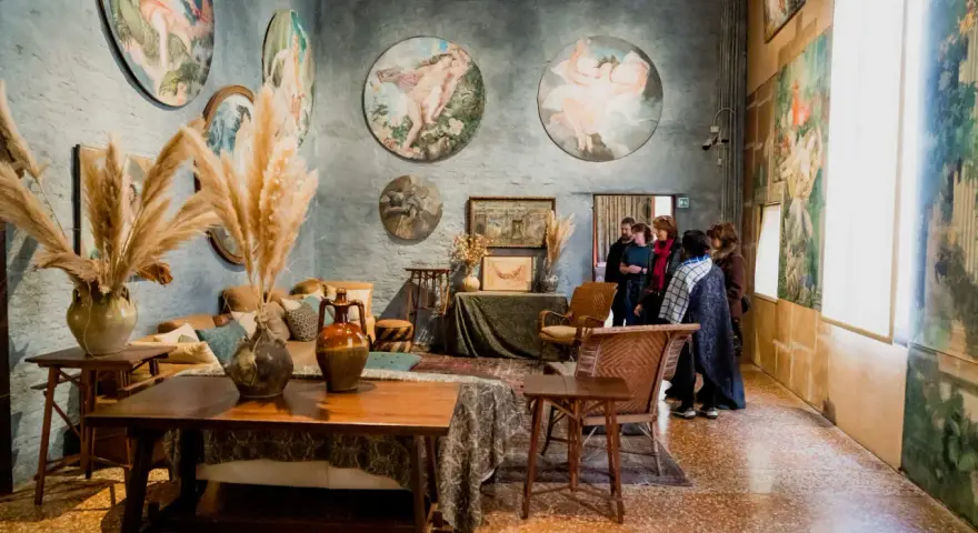 Interno del museo Palazzo Fortuny con opere d'arte alle pareti, arredi d'epoca e visitatori.