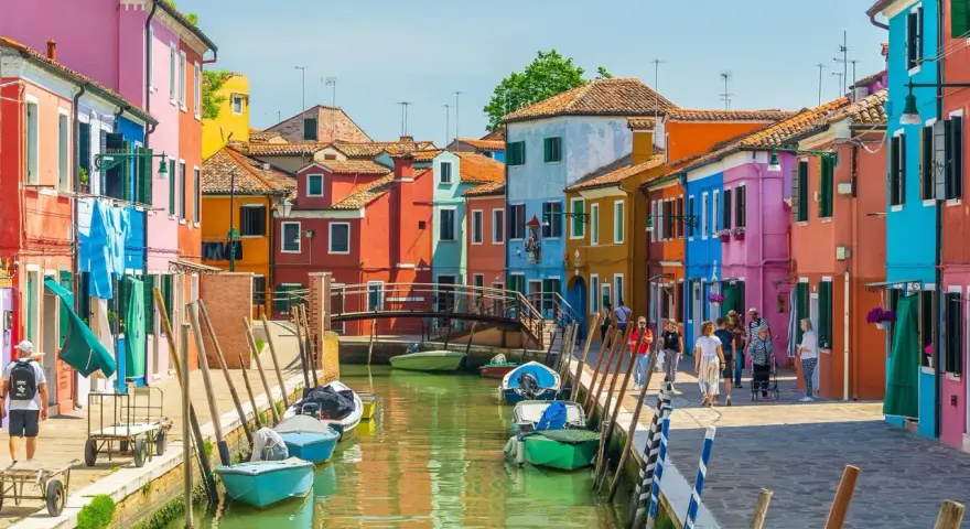 Colorate case affacciate su un canale a Venezia, con barche ormeggiate e persone che passeggiano. Le fondamenta sono un tripudio di colori vivaci.