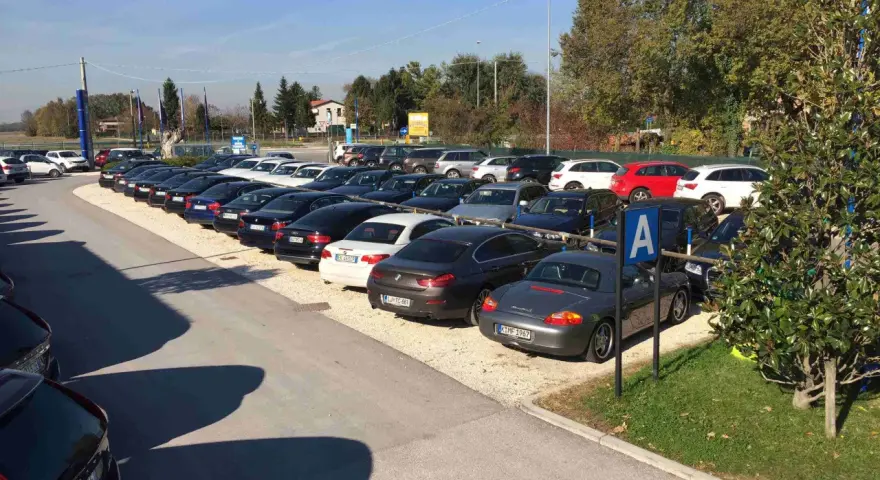 Parcheggio con auto moderne, forse vicino a Venezia Mestre o Santa Lucia. Un cartello blu con la "A" indica un'area di sosta.