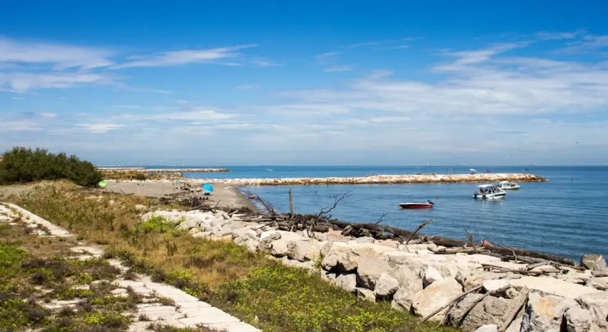 Sentiero in pietra e mare calmo con barche. Per capire come arrivare a Pellestrina da Fusina, immagina di percorrere questa costa.