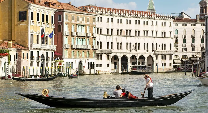 Gondola con turisti e gondoliere, sullo sfondo palazzi storici e altre barche tipiche veneziane.