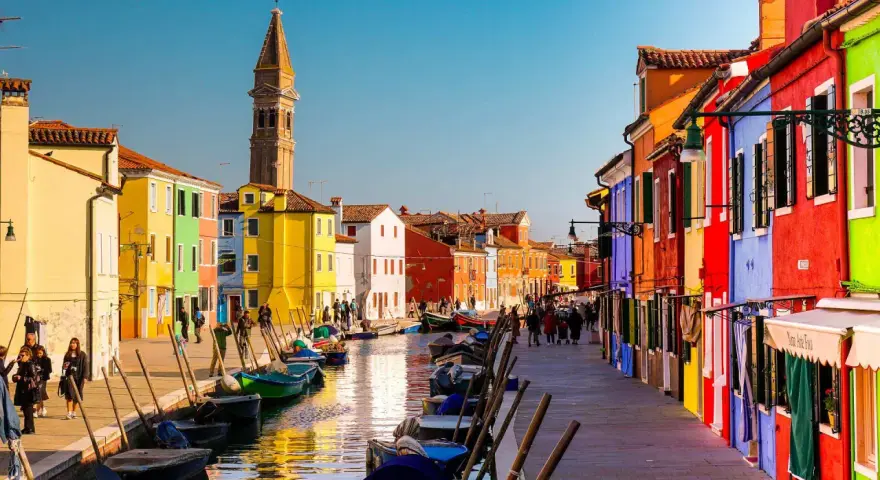 Coloratissima città lagunare con case vivaci, canali e barche ormeggiate.