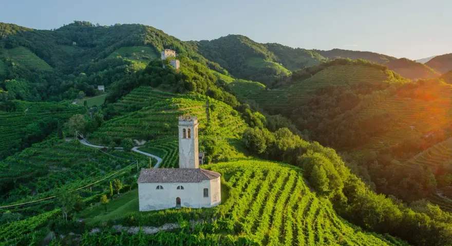 Un borgo con una chiesetta e campanile tra colline vitate, un esempio di cosa vedere nei dintorni di Treviso per un paesaggio incantevole.