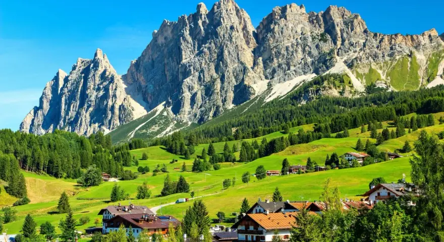 Un viaggio da Venezia a Cortina: verdi pascoli, boschi rigogliosi e imponenti vette dolomitiche incorniciano un villaggio alpino.