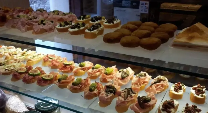 Vetrina piena di **migliori cicchetti Venezia**: crostini con affettati, fichi, olive e verdure. Un tripudio di sapori da gustare.