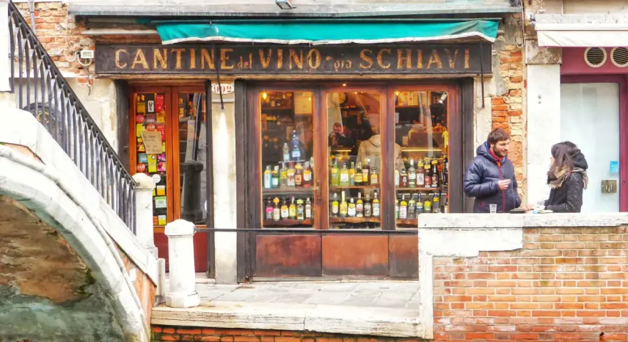 Coppia davanti a una delle tipiche osterie a Venezia, con bottiglie di vino in esposizione.