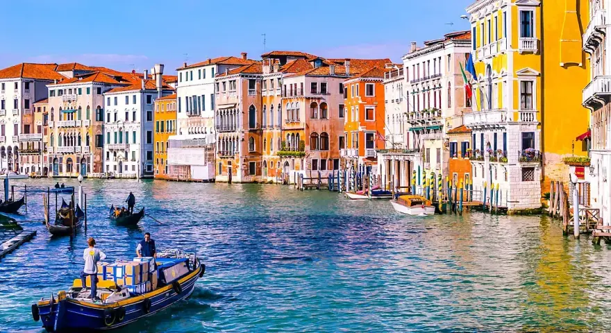 Venezia: turisti in gondola e vaporetti sul Canal Grande, tra palazzi colorati e acque azzurre.