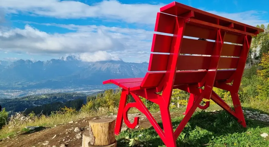 La panchina gigante sul Nevegal, rossa e imponente, domina un panorama mozzafiato di montagne e vallate sotto un cielo azzurro.