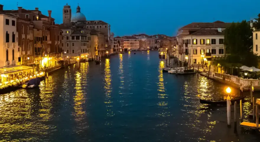 Serata magica per visitar Venezia: luci dorate sui palazzi e riflessi sull'acqua del Canal Grande, con gondole e ristoranti animati.