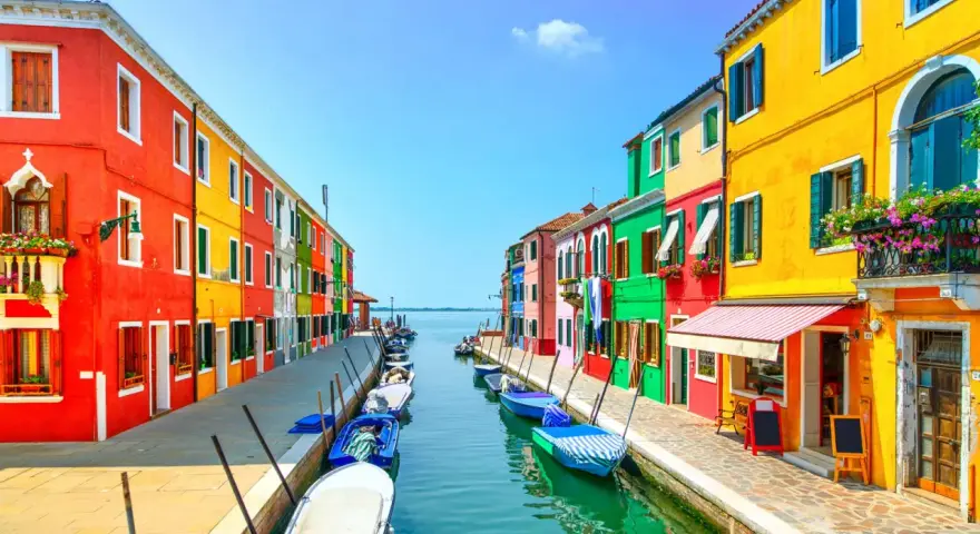 Coloratissima isola a Venezia, con case vivaci affacciate su un canale pieno di barche.