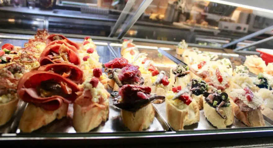 Assortimento di cicchetti in una vetrina di un'osteria veneziana: crostini con salumi, pesce e verdure.