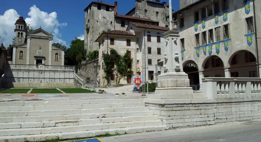 Piazza con scalinata, chiesa e castello: ecco cosa vedere a Feltre. Stendardi gialli decorano gli edifici storici.